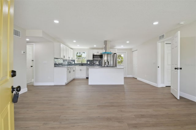 kitchen with white cabinetry, stainless steel appliances, a center island, light hardwood / wood-style floors, and decorative backsplash