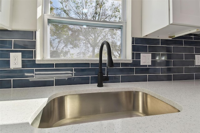 details featuring white cabinets, light stone countertops, sink, and backsplash