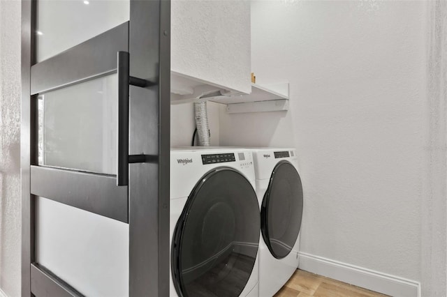 clothes washing area with washing machine and clothes dryer, light wood finished floors, baseboards, laundry area, and a textured wall