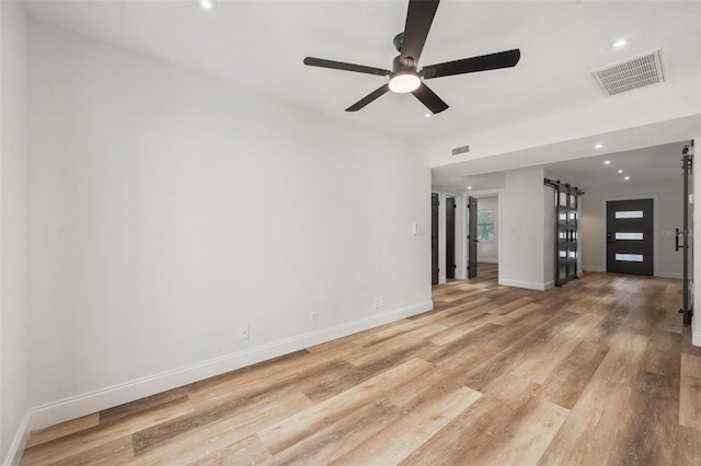 unfurnished living room featuring visible vents, baseboards, light wood-type flooring, a barn door, and a ceiling fan