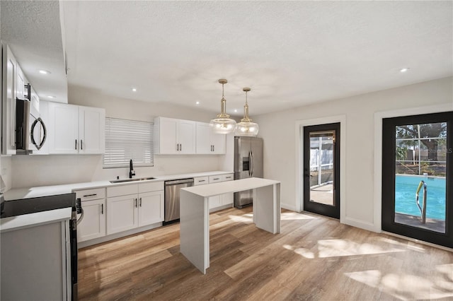 kitchen with light countertops, light wood-style floors, white cabinets, stainless steel appliances, and a sink