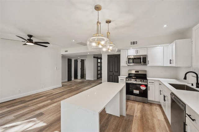 kitchen featuring visible vents, a kitchen island, a sink, light countertops, and appliances with stainless steel finishes