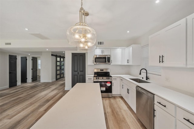 kitchen with visible vents, a barn door, light wood-style floors, stainless steel appliances, and a sink