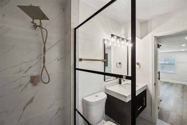 bathroom featuring vanity, wood finished floors, a marble finish shower, toilet, and a textured wall