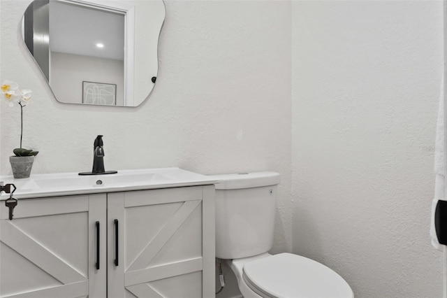 bathroom featuring vanity, toilet, and a textured wall