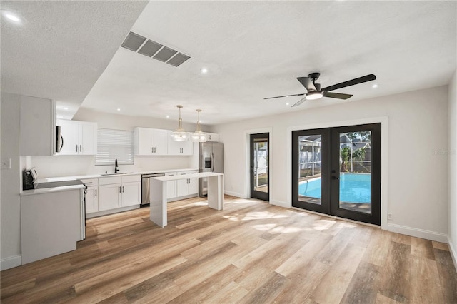 kitchen with visible vents, a kitchen island, appliances with stainless steel finishes, french doors, and a sink