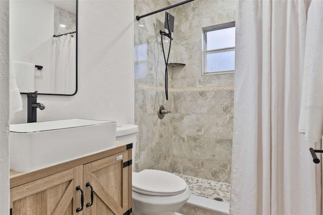 bathroom featuring vanity, toilet, a textured wall, and a tile shower