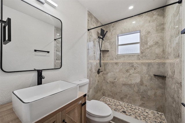 bathroom featuring a textured wall, toilet, vanity, and a tile shower