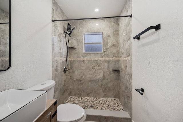 full bathroom featuring tiled shower, toilet, vanity, and a textured wall