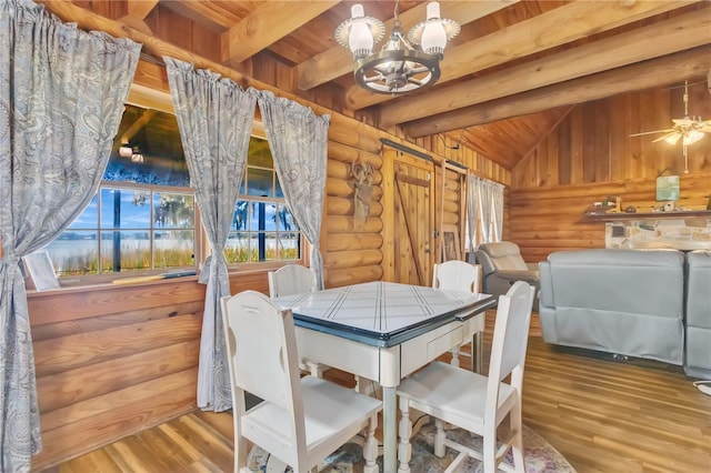 dining room with hardwood / wood-style floors, ceiling fan with notable chandelier, lofted ceiling with beams, and rustic walls