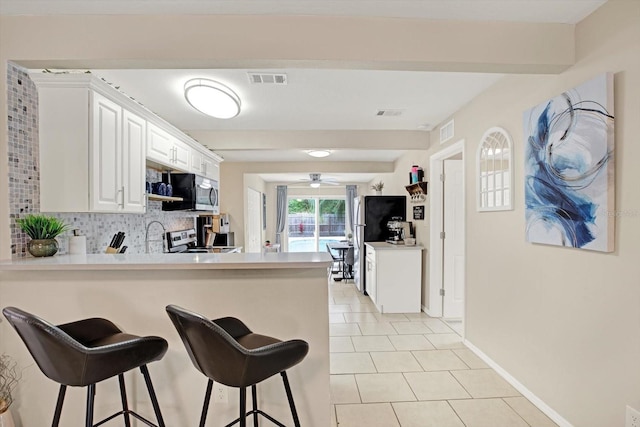 kitchen with tasteful backsplash, appliances with stainless steel finishes, white cabinets, and kitchen peninsula