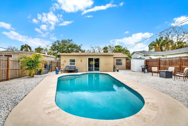 view of pool with a storage shed, a fire pit, a patio, and a grill