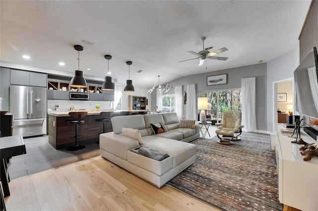 living room featuring lofted ceiling, ceiling fan with notable chandelier, light hardwood / wood-style flooring, and a textured ceiling