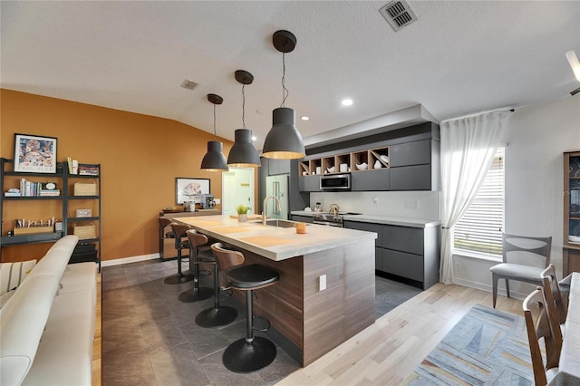 kitchen featuring sink, vaulted ceiling, a center island with sink, appliances with stainless steel finishes, and pendant lighting