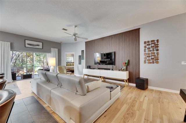 living room with ceiling fan, light hardwood / wood-style floors, and a textured ceiling