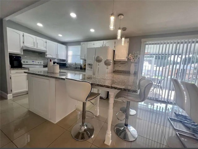 kitchen featuring tile patterned flooring, a breakfast bar, white cabinets, and white appliances