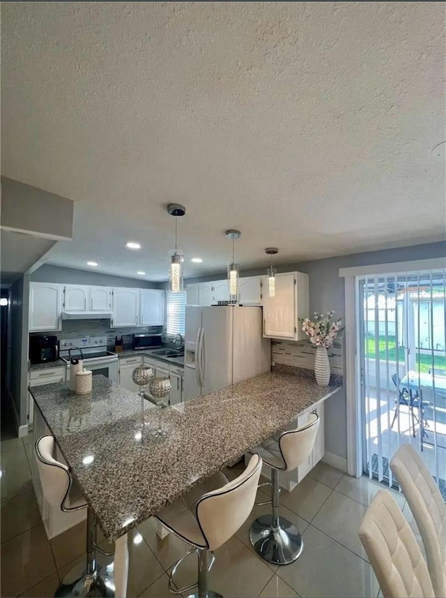 kitchen featuring white cabinetry, a breakfast bar area, light tile patterned floors, kitchen peninsula, and white appliances