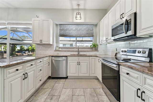 kitchen with sink, dark stone countertops, stainless steel appliances, white cabinets, and decorative light fixtures