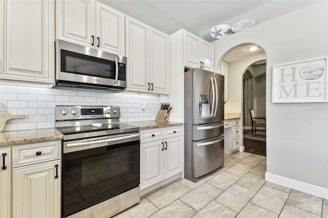 kitchen with light tile patterned floors, backsplash, stainless steel appliances, light stone countertops, and white cabinets