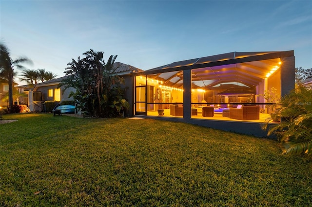 back house at dusk with a lawn, outdoor lounge area, a patio, and glass enclosure