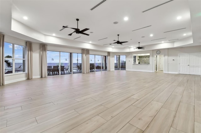 unfurnished living room with a raised ceiling, ceiling fan, and light wood-type flooring