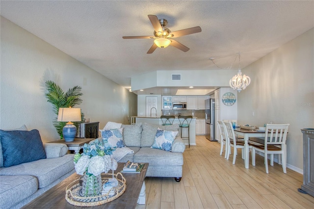 living room with sink, ceiling fan with notable chandelier, a textured ceiling, and light wood-type flooring