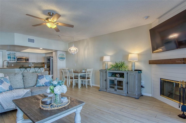 living room with sink, a textured ceiling, a large fireplace, ceiling fan, and light hardwood / wood-style floors