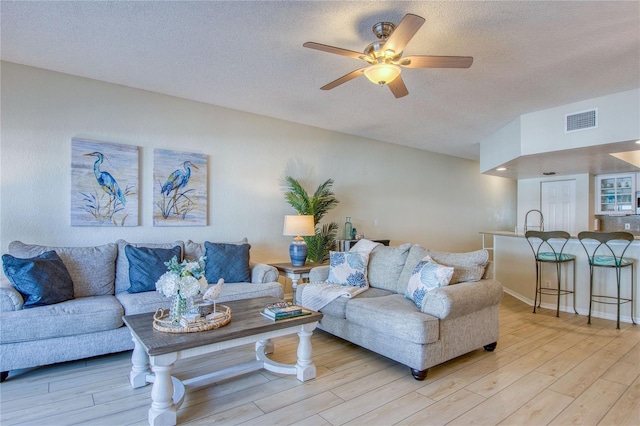 living room with ceiling fan, sink, light hardwood / wood-style flooring, and a textured ceiling