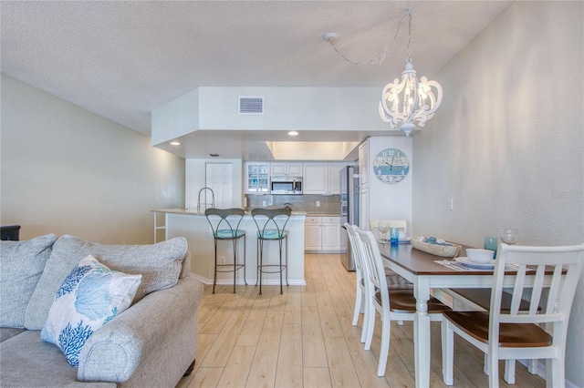 dining space featuring lofted ceiling, sink, a chandelier, a textured ceiling, and light hardwood / wood-style flooring