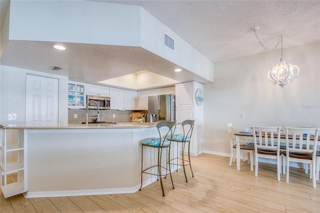 kitchen featuring a breakfast bar, appliances with stainless steel finishes, white cabinetry, decorative backsplash, and light wood-type flooring