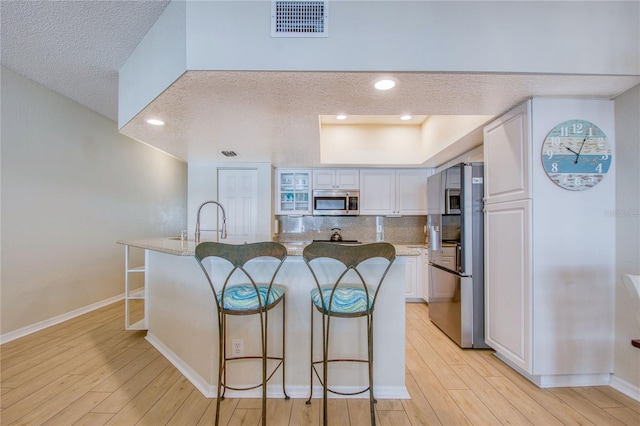 kitchen with appliances with stainless steel finishes, a kitchen bar, an island with sink, and white cabinets