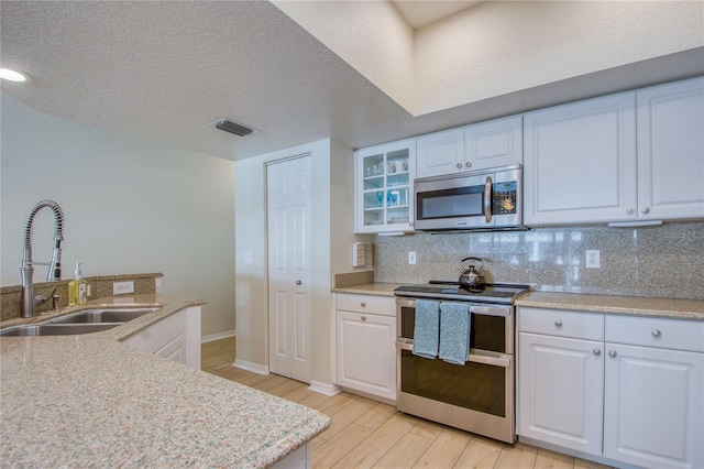 kitchen with appliances with stainless steel finishes, sink, white cabinets, decorative backsplash, and light wood-type flooring