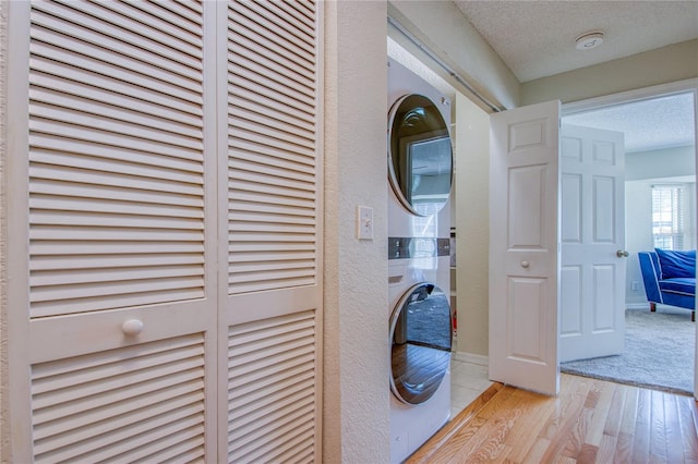 laundry area with stacked washer and clothes dryer, a textured ceiling, and light wood-type flooring