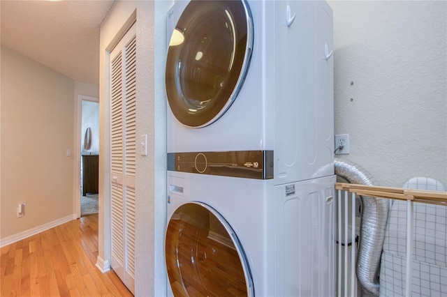 laundry room featuring stacked washer / dryer, a textured ceiling, and light hardwood / wood-style floors