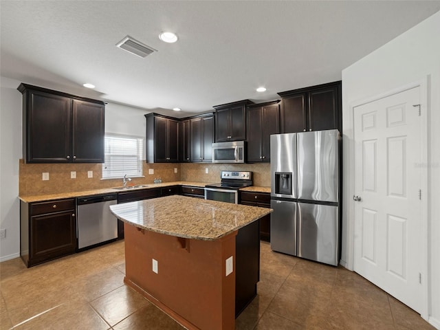 kitchen featuring tasteful backsplash, light stone counters, a center island, dark brown cabinets, and appliances with stainless steel finishes