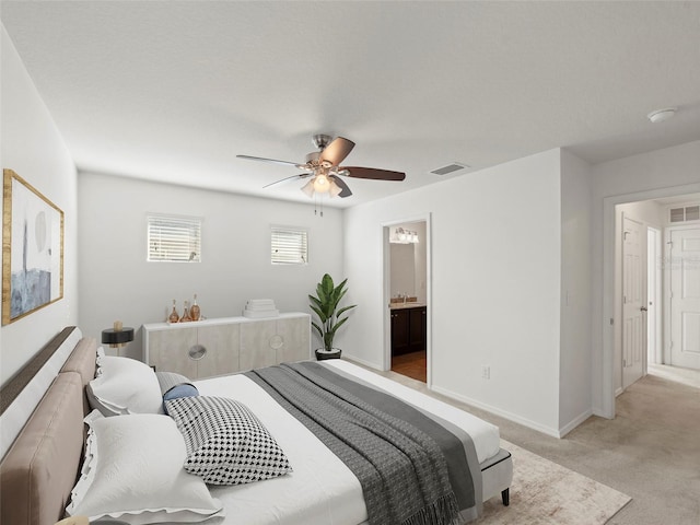 bedroom with ensuite bathroom, light carpet, and ceiling fan