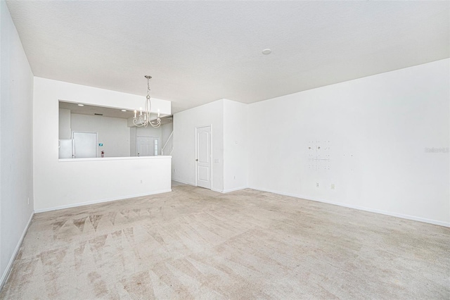 spare room with light carpet, a chandelier, and a textured ceiling