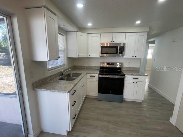 kitchen with stainless steel appliances, white cabinetry, light stone countertops, and sink