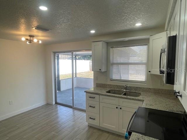 kitchen with sink, light stone counters, white cabinets, light hardwood / wood-style floors, and stove