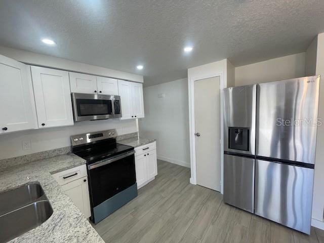 kitchen featuring appliances with stainless steel finishes, light wood-type flooring, white cabinets, and light stone counters