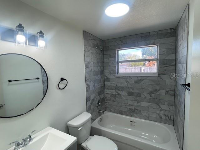 full bathroom with vanity, toilet, tiled shower / bath combo, and a textured ceiling