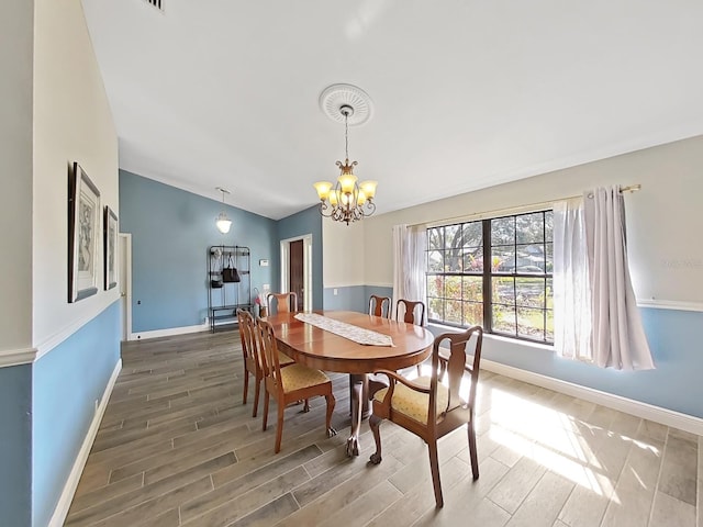 dining area with hardwood / wood-style flooring, an inviting chandelier, and vaulted ceiling