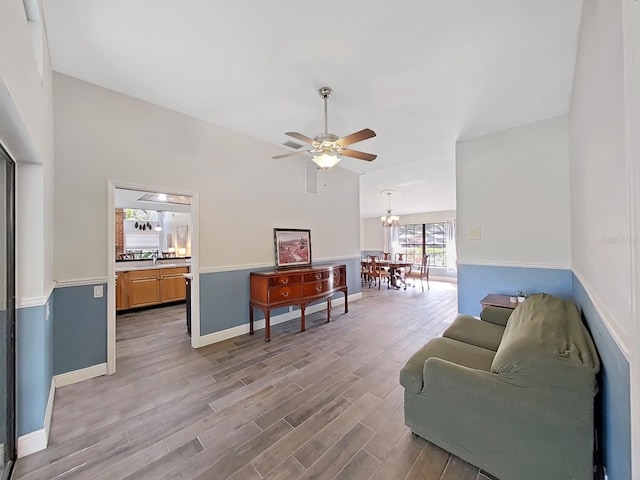 living area with lofted ceiling, sink, ceiling fan with notable chandelier, and light hardwood / wood-style flooring