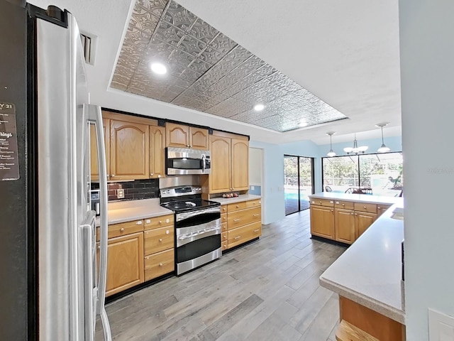 kitchen featuring decorative light fixtures, stainless steel appliances, decorative backsplash, and light wood-type flooring