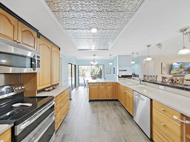 kitchen with appliances with stainless steel finishes, decorative light fixtures, sink, light hardwood / wood-style floors, and kitchen peninsula