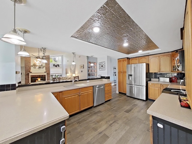 kitchen with sink, hanging light fixtures, a brick fireplace, a tray ceiling, and stainless steel appliances