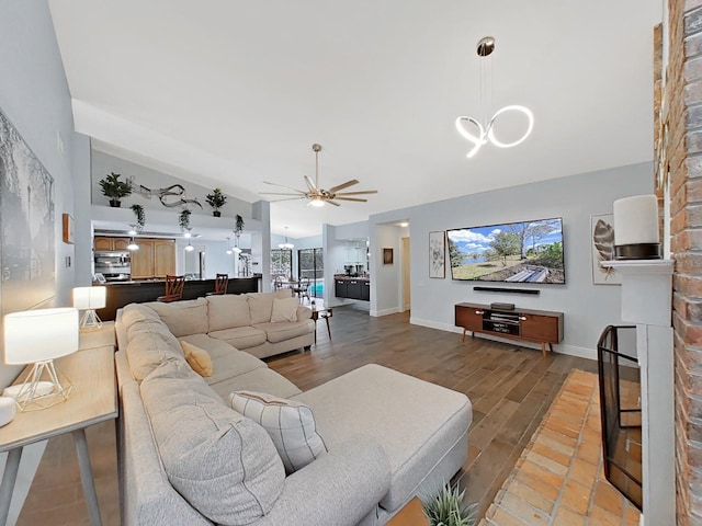 living room with vaulted ceiling, ceiling fan with notable chandelier, a large fireplace, and hardwood / wood-style floors