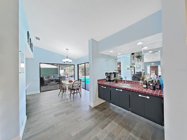 kitchen with sink, a chandelier, vaulted ceiling, hanging light fixtures, and hardwood / wood-style floors