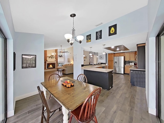 dining room featuring dark wood-type flooring, a fireplace, and ceiling fan with notable chandelier