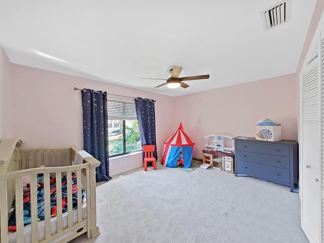 bedroom featuring a crib, light colored carpet, and ceiling fan